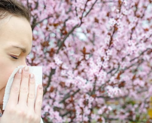 Woman blowing nose with flowers in background.